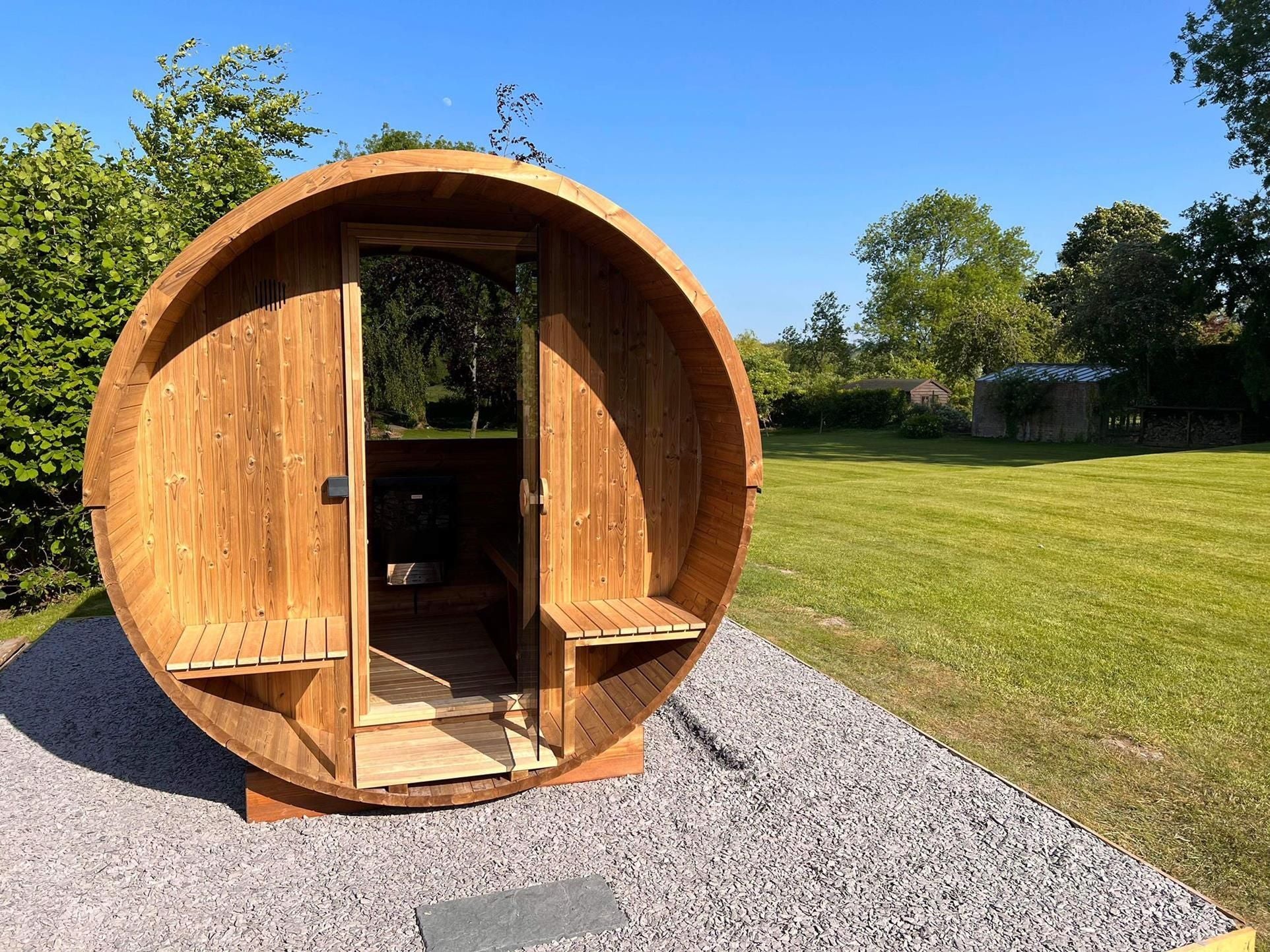 Hekla Barrel Sauna 250 outdoor sauna cabin, front view on grass (lifestyle image).