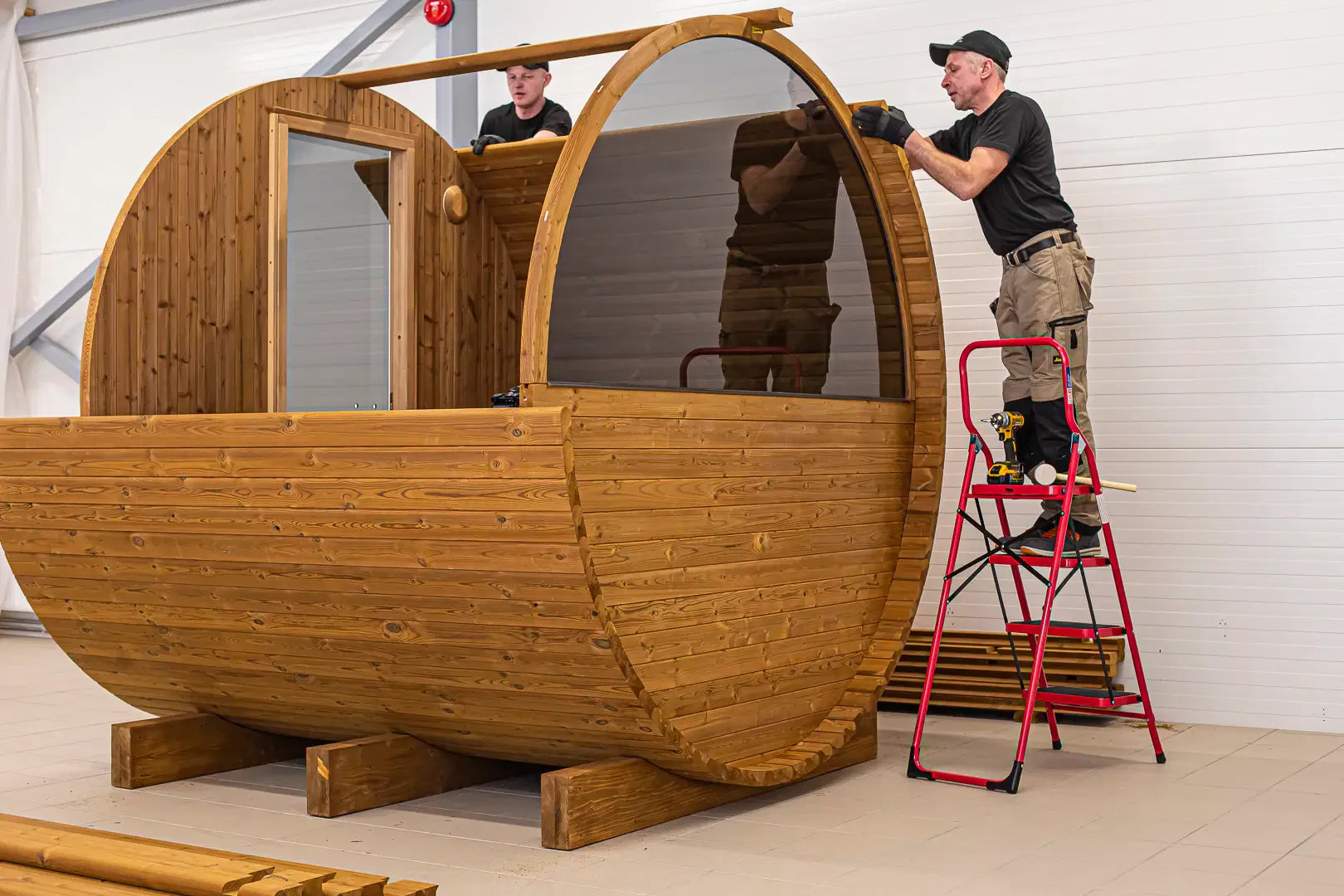 Factory assembly image showing barrel sauna frame installation.